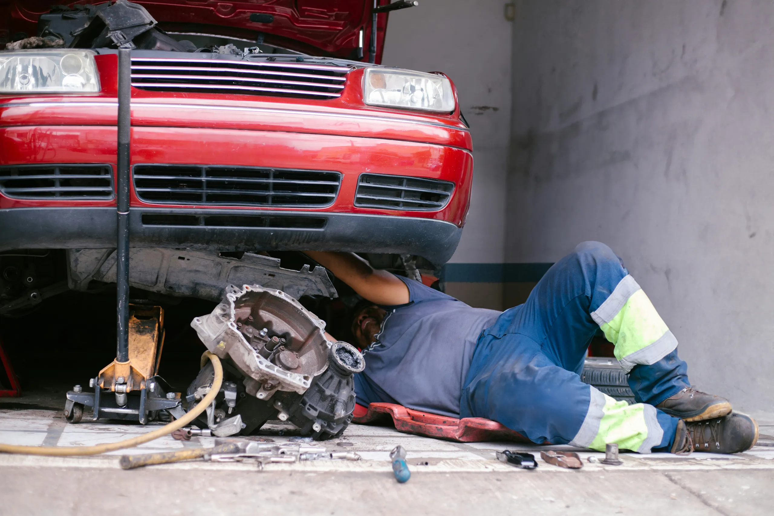 Mecánico tumbado bajo un coche elevado montando la caja de cambios