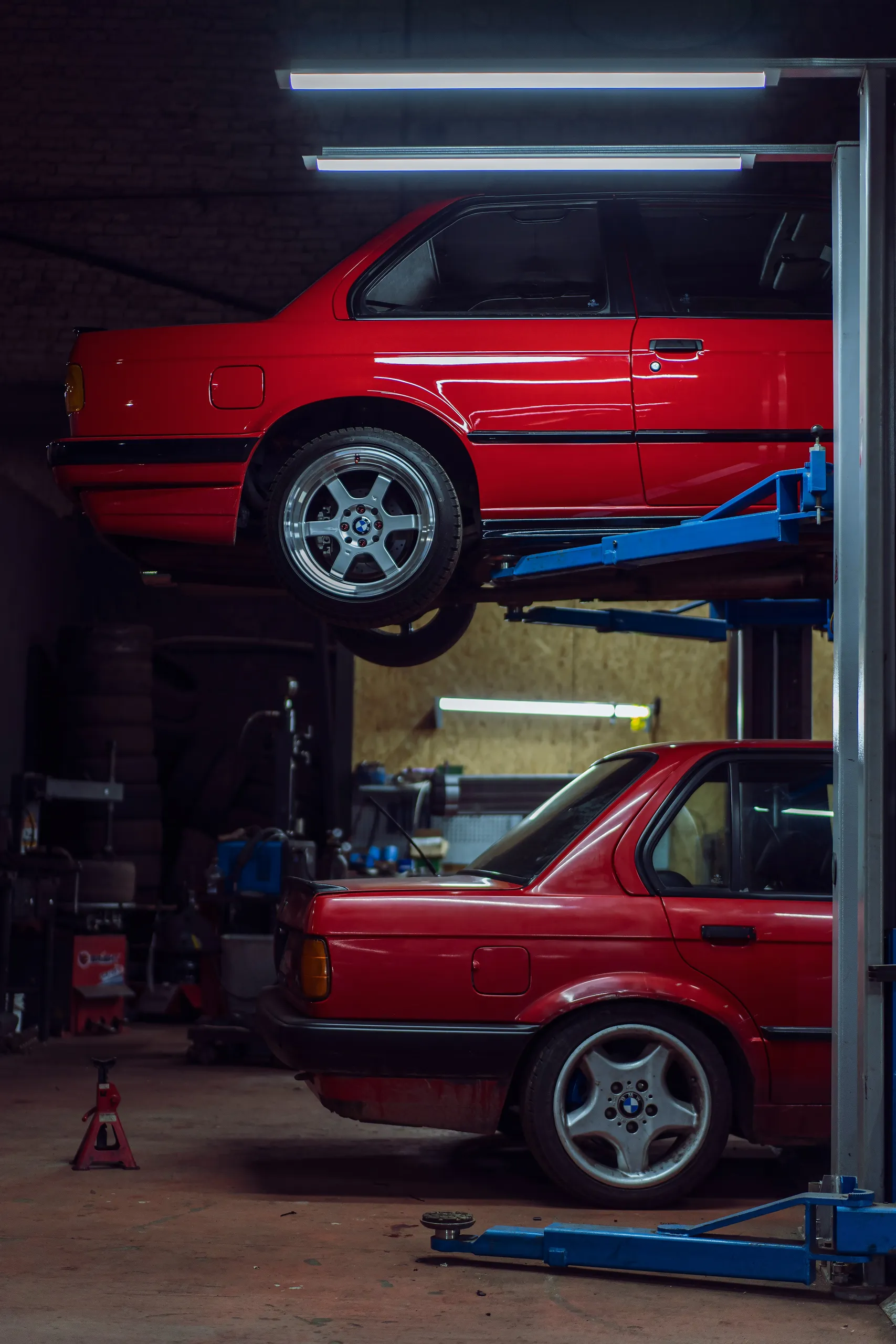 Dos BMW E30 rojos, uno sobre el elevador en el taller durante una reparación
